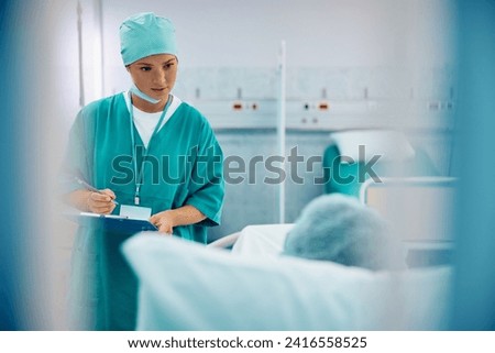 Female surgeon taking notes while visiting her patient who is recovering in hospital ward. Copy space.