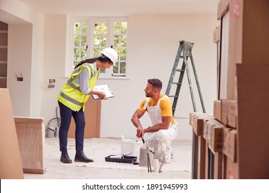 Female Surveyor With Clipboard Meeting With Decorator Working Inside Property