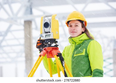 female surveyor worker working with theodolite transit equipment at building construction site outdoors