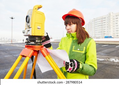 female surveyor worker working with theodolite transit equipment at road construction site outdoors