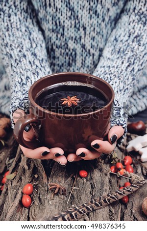 A female in sweater is warming up herself with a mug of hot tea outdoors