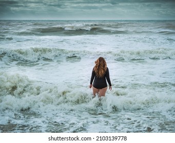 Female Swimmer With Long Hair Wearing Wet Suit Walking Into Rough Sea 