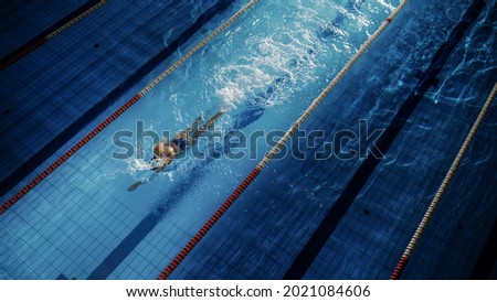 Female Swimmer Racing in Swimming Pool. Professional Athlete Overcoming Stress and Hardships in Dark Dramatic Pool, Cinematic Lap Lane Light Showing the Good Way. Aerial Shot