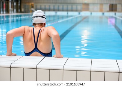 Female swimmer relaxs on the side of the swimmingpool wearing a white swimming cap
