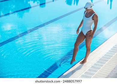 Female swimmer in white swim cap and goggles standing on poolside outdoors, showcasing athleticism, preparation, and outdoor swimming - Powered by Shutterstock