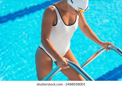 Female swimmer in white swim cap and goggles standing on poolside outdoors, showcasing athleticism, preparation, and outdoor swimming - Powered by Shutterstock