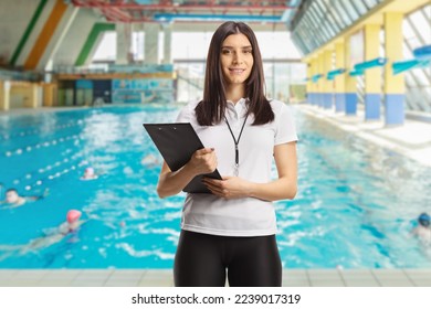 Female swimming coach with a whistle holding a clipboard and posing on an indoors swimming pool - Powered by Shutterstock