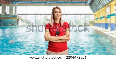 Female swimming coach with a wistle and stopwatch around her neck posing on an indoors swimming pool