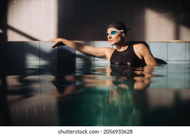 Female Swimming Instructor Is Posing In Goggles, Black Swimming Suit And A Cap In A Sports Centre