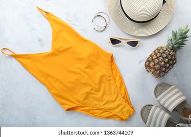 Female swimming suit, hat, pineapple and beach shoes on light background. Travel concept