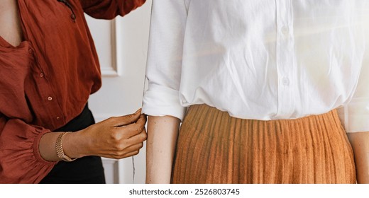 Female tailor adjusts the sleeve of a white shirt. The tailor works on ensuring the sleeve fits perfectly. The white shirt is being tailored. Fashion designer measuring a shirt for perfect fit. - Powered by Shutterstock