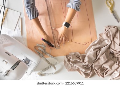 Female tailor hands draw sew pattern ruler and felt tip pen on desk clothes creating workshop top view closeup. Woman dressmaker fashion designer tailoring dressmaking with sewing machine at studio