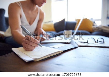 Female taking notes whilst working from home.