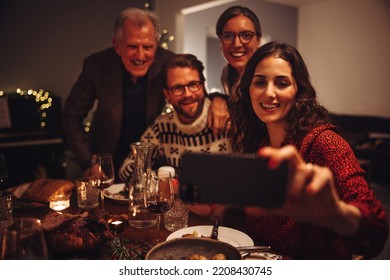 Female taking selfies with family on christmas eve dinner. Family taking selfie during Christmas dinner at home.