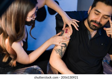 Female tattoo artist covering the new tattoo of a hipster young man with plastic film to protect it  - Powered by Shutterstock