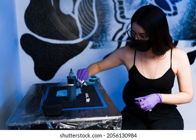 Female Tattoo Artist With A Face Mask Preparing The Ink At Her Shop To Start Tattooing