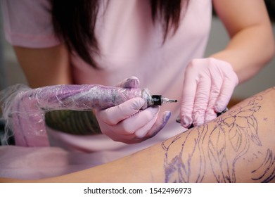 Female Tattoo Master Tattooing Female Client. Figure Nuns On The Thigh. Pink Tattoo Machine And Lamp. Workplace Artist.