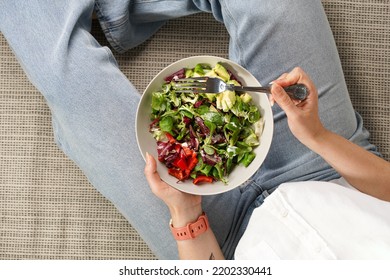 Female with tattoos wearing blue jeans and white shirt sitting and holding a grey bowl with salad and a fork ready to eat, healthy life style concept - Powered by Shutterstock