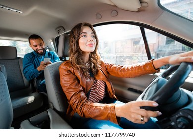 Motorista de táxi dirigindo um carro com passageiro do sexo masculino sentado ao fundo e usando telefone inteligente.