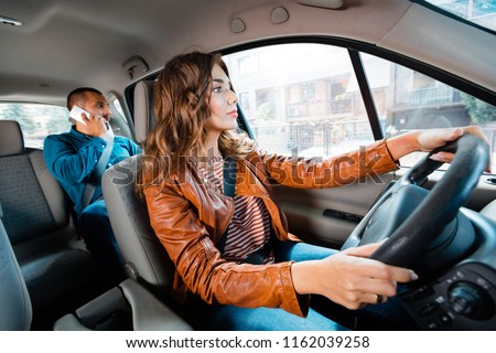 Female taxi driver driving a car with male passenger talking on mobile phone in the background. 