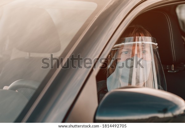 Female taxi driver with protective face mask and\
plastic visor waiting in\
car