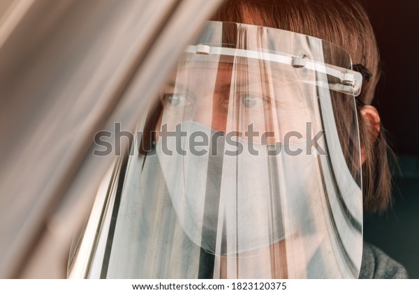Female taxi driver with protective face mask and\
plastic visor waiting in\
car