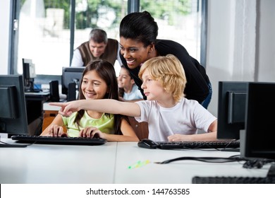 Female Teacher Assisting Boy Pointing On Computer In Lab At School