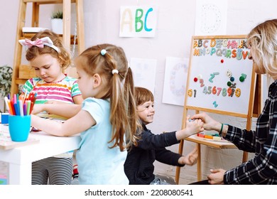 Female Teacher With Children Have Fun In Kid Development Center. Paintings, Art, Math And English Language Lessons. Nursery School And Early Education For Foster Families, Adoption And Child Care.