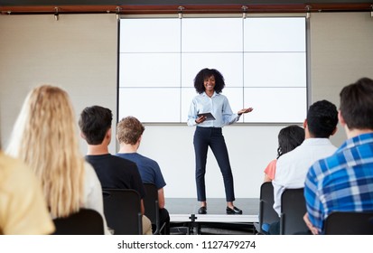 Female Teacher With Digital Tablet Giving Presentation To High School Class In Front Of Screen