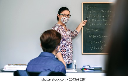 Female Teacher With Face Mask In Math Class With Student Raising Hand