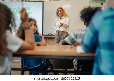 Female teacher gesturing while explaining a lesson to her elementary school multi ethnic students sitting at desks in the classroom