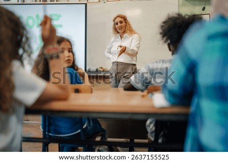 Female teacher gesturing while explaining a lesson to her elementary school multi ethnic students sitting at desks in the classroom