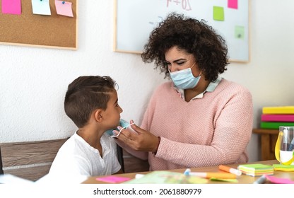 Female Teacher Giving Face Protective Mask To Student In Preschool Classroom During Corona Virus Pandemic - Healthcare And Education Concept