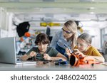 Female teacher helping to girls working on small robot, building robotic car in after-school robotics club. Children learning robotics in Elementary school. Girls in science.