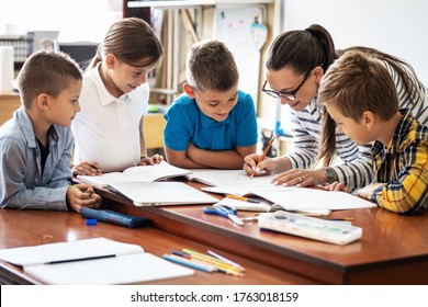 Female teacher helps school kids to finish they lesson.They sitting all together at one desk. - Shutterstock ID 1763018159