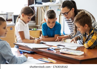 Female teacher helps school kids to finish they lesson.They sitting all together at one desk. - Shutterstock ID 1763018162