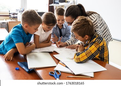 Female teacher helps school kids to finish they lesson.They sitting all together at one desk. - Shutterstock ID 1763018165