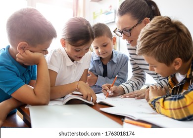 Female teacher helps school kids to finish they lesson.They sitting all together at one desk. - Shutterstock ID 1763018174