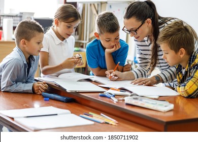 Female teacher helps school kids to finish they lesson.They sitting all together at one desk.	
 - Shutterstock ID 1850711902