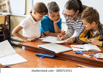 Female teacher helps school kids to finish they lesson.They sitting all together at one desk.	
 - Shutterstock ID 1850711911