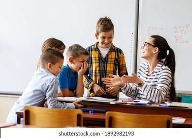 Female Teacher Helps School Kids To Finish They Lesson.They Sitting All Together At One Desk.