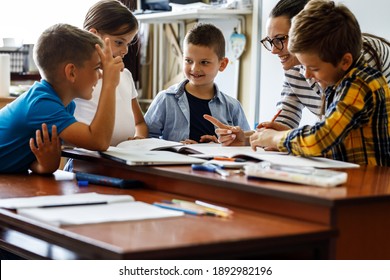Female teacher helps school kids to finish they lesson.They sitting all together at one desk.