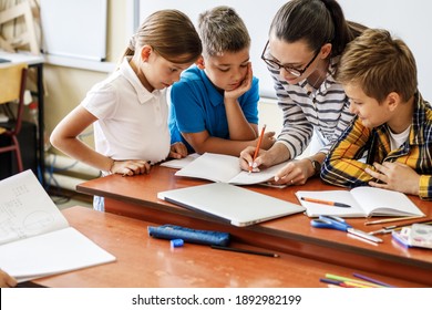 Female teacher helps school kids to finish they lesson.They sitting all together at one desk.