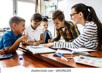 Female Teacher Helps School Kids To Finish They Lesson.They Sitting All Together At One Desk.