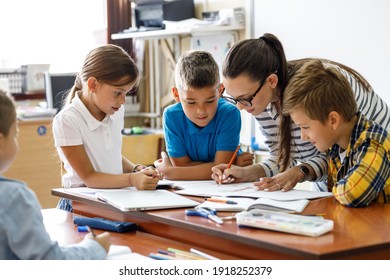 Female teacher helps school kids to finish they lesson.They sitting all together at one desk.	
 - Shutterstock ID 1918252379