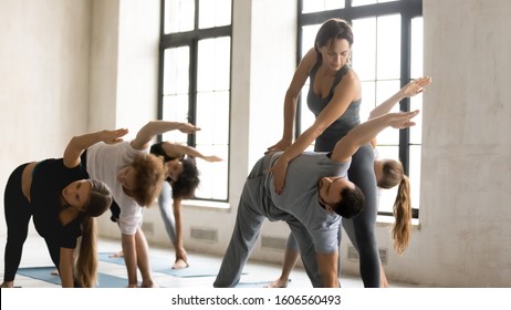 Female Teacher Instructor Training Man, Doing Utthita Trikonasana Exercise At Group Lesson, Practicing Yoga, Stretching In Extended Triangle Pose, Working Out In Modern Yoga Studio, Center