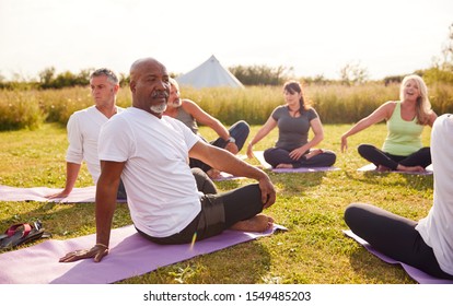 Female Teacher Leading Group Of Mature Men And Women In Class At Outdoor Yoga Retreat