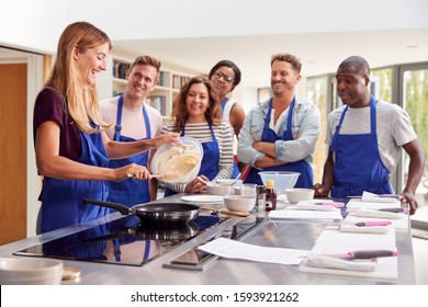 Female Teacher Making Pancake On Cooker In Cookery Class As Adult Students Look On