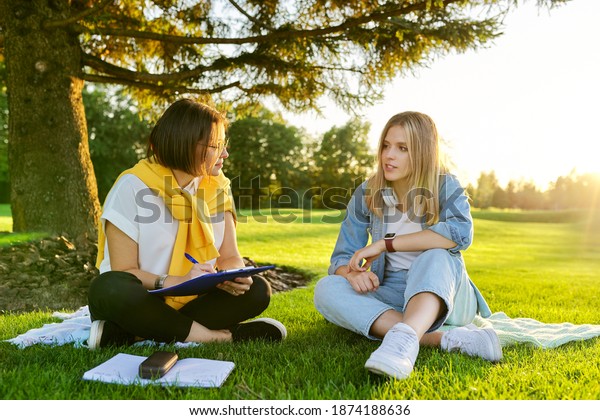 Female teacher psychologist social worker talking\
to teenage student on the lawn in the park. Sociology, psychology,\
education, youth concept