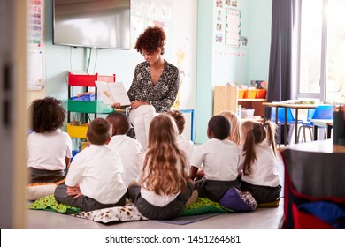 Female Teacher Reading Story To Group Of Elementary Pupils Wearing Uniform In School Classroom - Shutterstock ID 1451264681